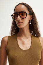 Close-up of model wearing the moss Hayes Knit with sunglasses, showing the narrow scoop neckline, wide shoulder straps and fine ribbed texture, front view
