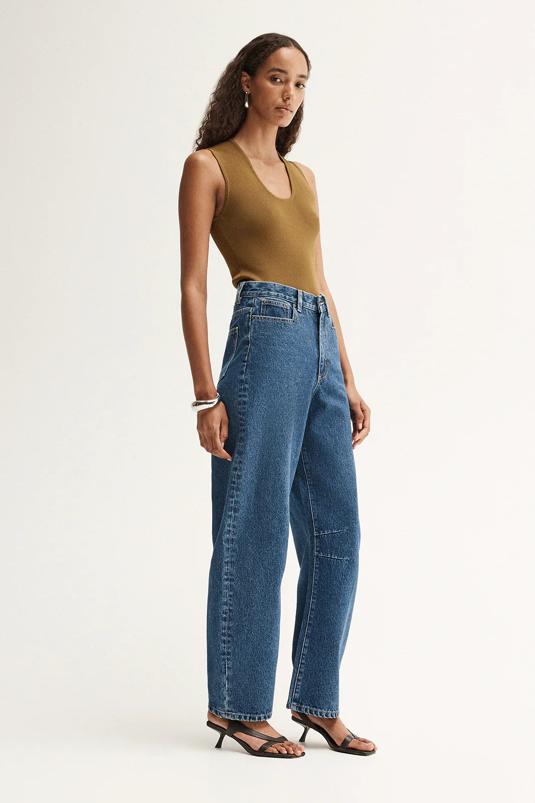 Model wearing the moss Hayes Knit with blue wide-leg jeans, showing the slim fit, sleeveless silhouette and hip-length finish, full-length angled view
