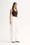 A model in a chocolate-brown sleeveless ribbed top and white wide-leg trousers, photographed from an angled front view that shows the scoop neckline and slim fit through the body.
