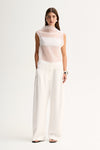 A woman wearing a white sheer mock-neck top with a layered inner slip, styled with wide-leg white trousers in a full-length front view.