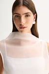 Close-up front view showing the white sheer fabric, mock neckline and layered inner panel of the top.