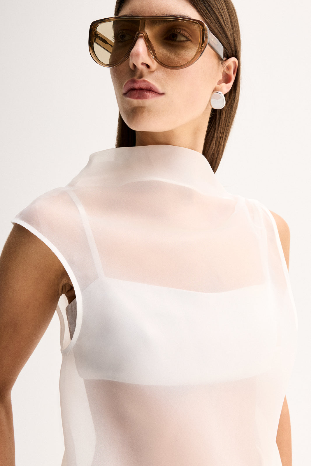 Close-up view of a woman wearing the white sheer mock-neck top with oversized sunglasses, highlighting the layered neckline and sleeveless design.