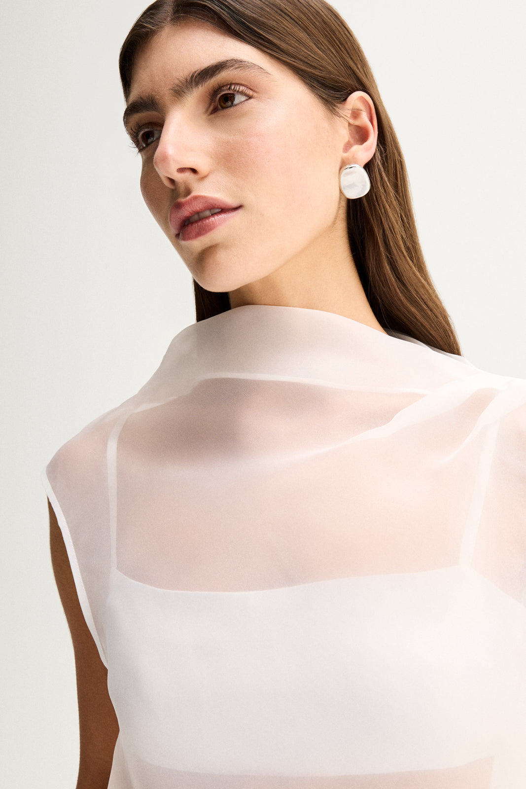 Close-up three-quarter view showing the white sheer mock-neck top, layered inner panel and clean sleeveless line.