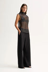 A model wears the black high-neck top with wide-leg trousers in an angled front studio view.
