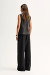 A model wears the sheer black sleeveless top in a back studio view with wide-leg trousers.
