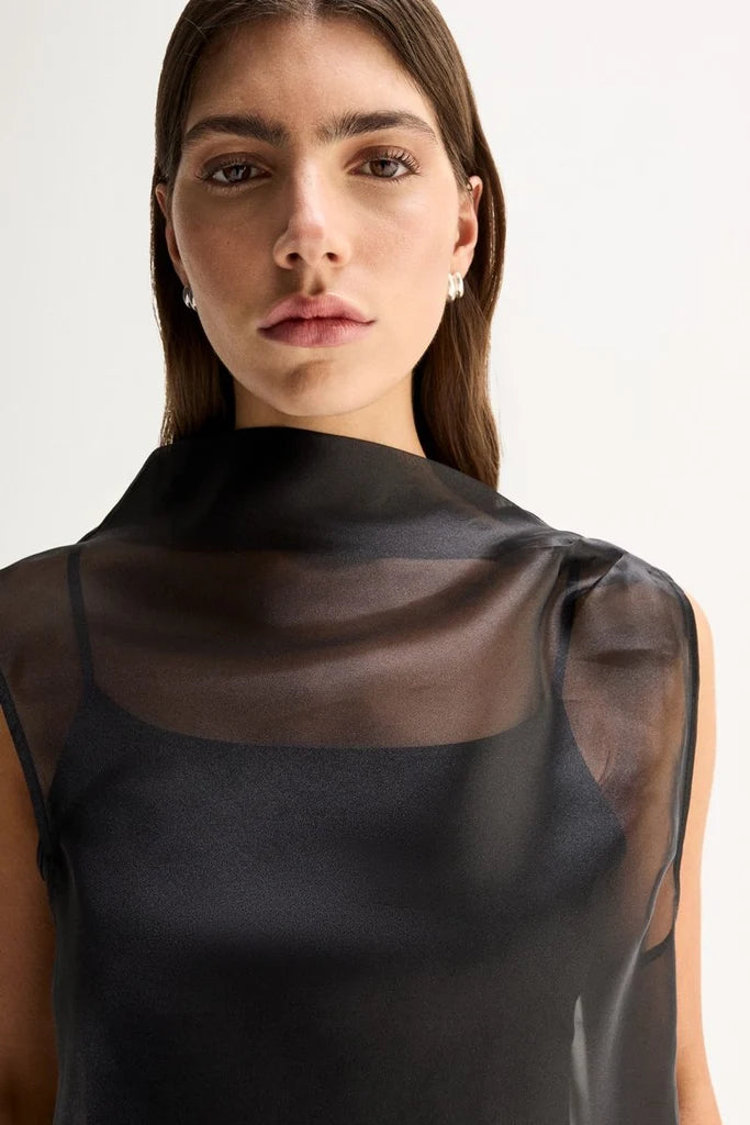 A close-up shows the sheer black sleeveless top with a softly draped high neckline and visible camisole underneath.
