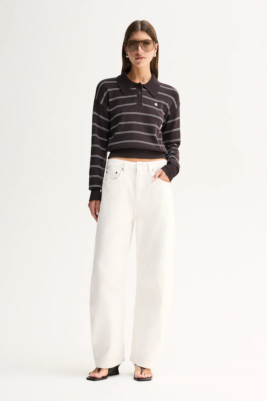 A model wearing a black and white horizontally striped long-sleeve polo crop top, paired with high-waisted white wide-leg jeans and black sandals, standing against a plain white studio background.