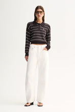 A model wearing a black and white horizontally striped long-sleeve polo crop top, paired with high-waisted white wide-leg jeans and black sandals, standing against a plain white studio background.