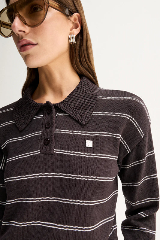 A close-up of a woman wearing a dark brown ribbed knit polo sweater with thin white horizontal stripes and a small white square logo patch on the chest.