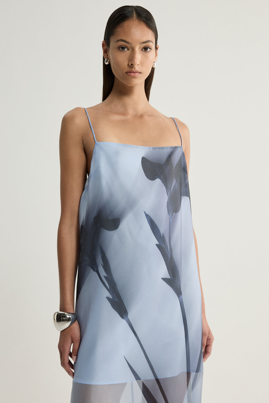 A closer front view of a pale blue dress showing its fine shoulder straps, straight neckline and oversized dark floral print across the bodice.
