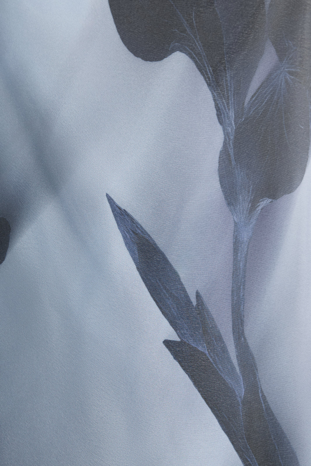 A close-up of sheer pale blue fabric with large dark floral shapes, revealing the fine translucent organza texture and layered print details.