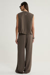 A rear view of a taupe sleeveless vest showing its simple back panel, shoulder seams and cropped hem, styled with matching wide-leg trousers.
