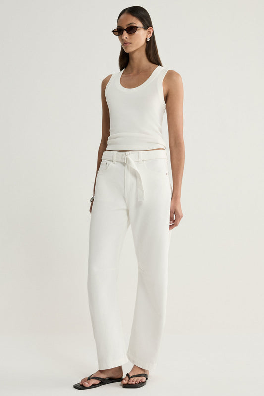 A model wearing ivory wide-leg denim pants with a tied waist belt and front pockets, paired with a white sleeveless top and black sandals in an angled front pose.