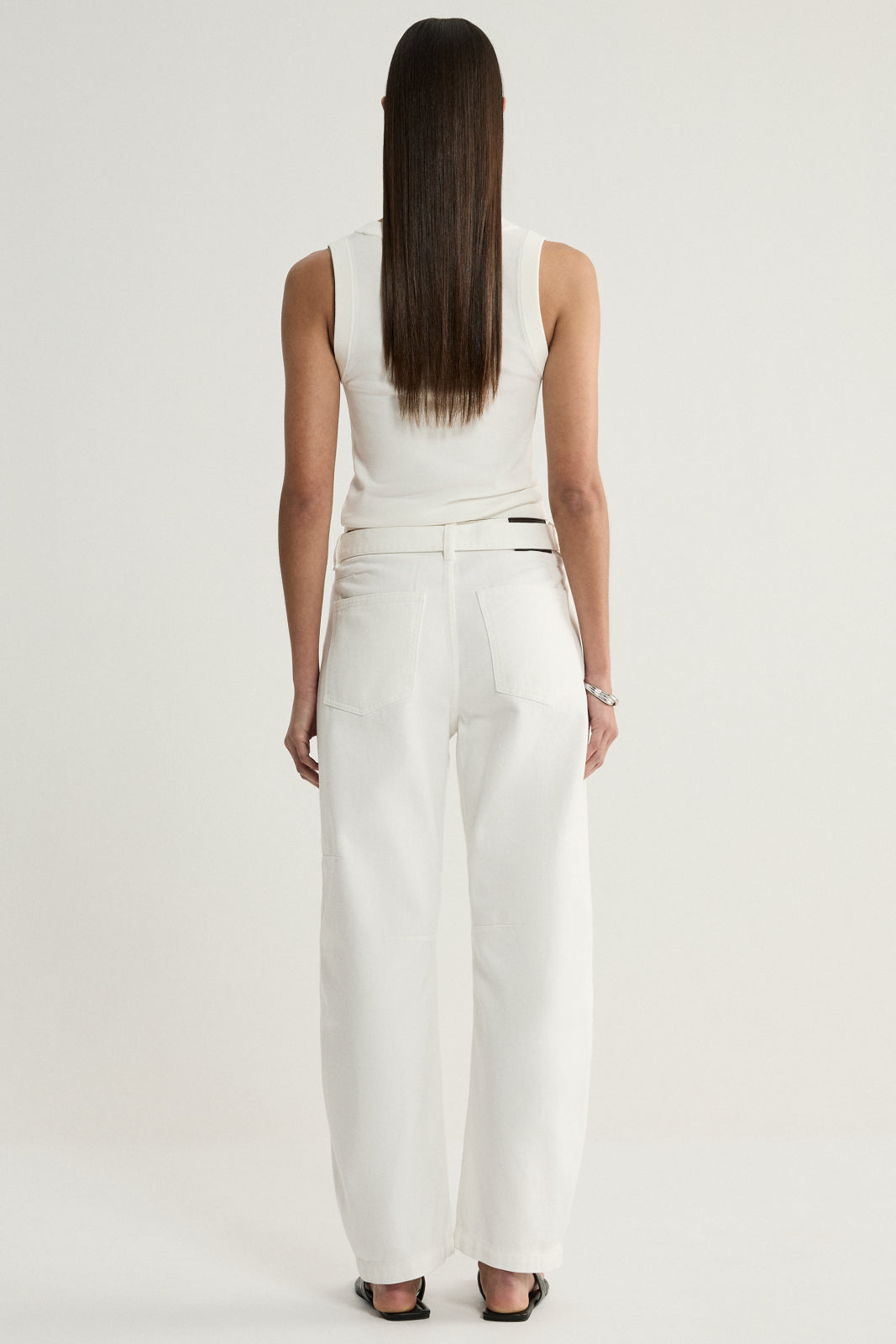 A rear view of a model wearing ivory wide-leg denim pants, showing the back pockets, waistband and long straight legs, paired with a white sleeveless top.