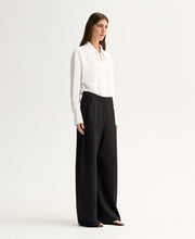 Model wearing the Ivory Elka Collective Millicent Shirt with black wide-leg trousers, showing the sharp point collar and deep V-neckline with silver-tone hardware, full-length angled view