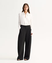 Model wearing the Ivory Elka Collective Millicent Shirt with black wide-leg trousers, showing the sharp point collar, open V-neckline and elegant wide cuffs, full-length front view