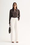 A woman wearing a slate long-sleeve shirt with a collared neckline and white wide-leg trousers in a full-length front view.
