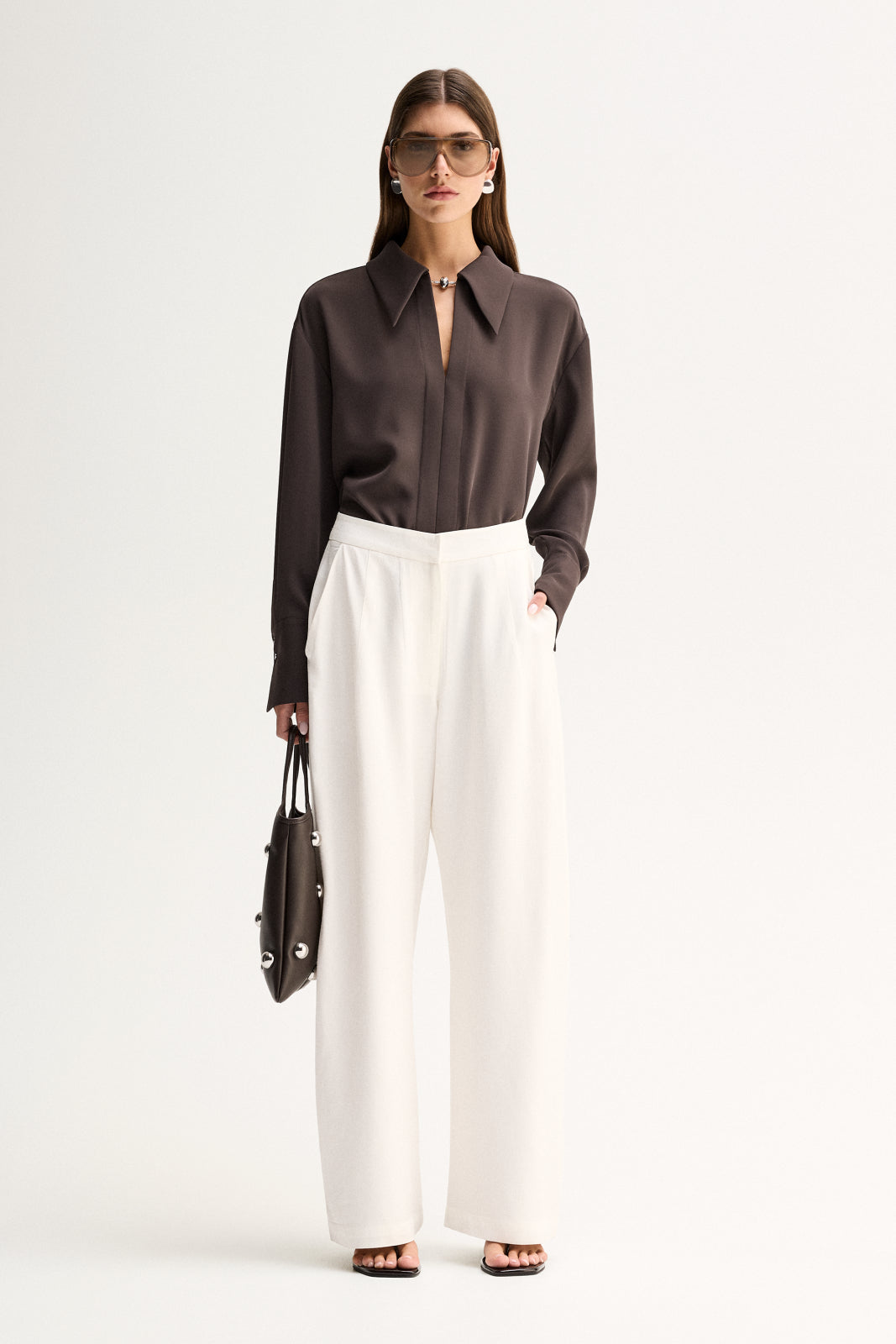 A woman wearing a slate long-sleeve shirt with a collared neckline and white wide-leg trousers in a full-length front view.