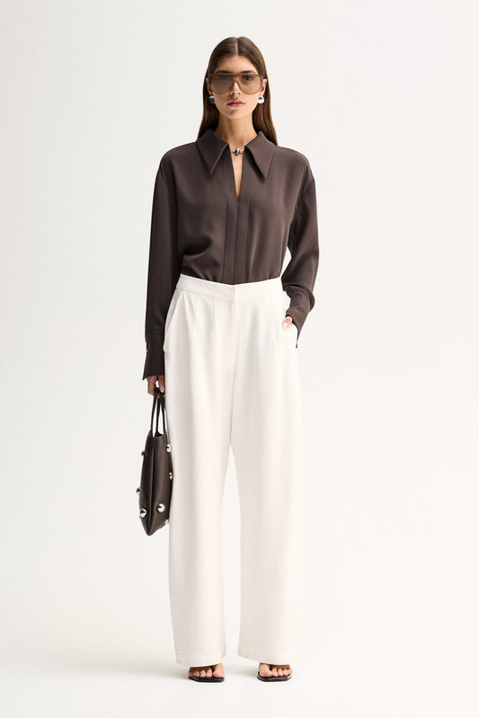 A woman wearing a slate long-sleeve shirt with a collared neckline and white wide-leg trousers in a full-length front view.