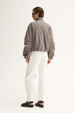 Person wearing a gray jacket and white pants on a white background