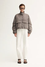 Person wearing a gray jacket and white pants on a white background
