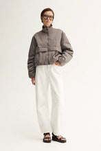 Person wearing a gray jacket and white pants on a white background