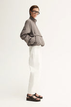 Person wearing a gray jacket, white pants, and black sandals on a white background