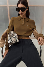 Woman wearing a brown sweater and sunglasses, holding a patterned bag.