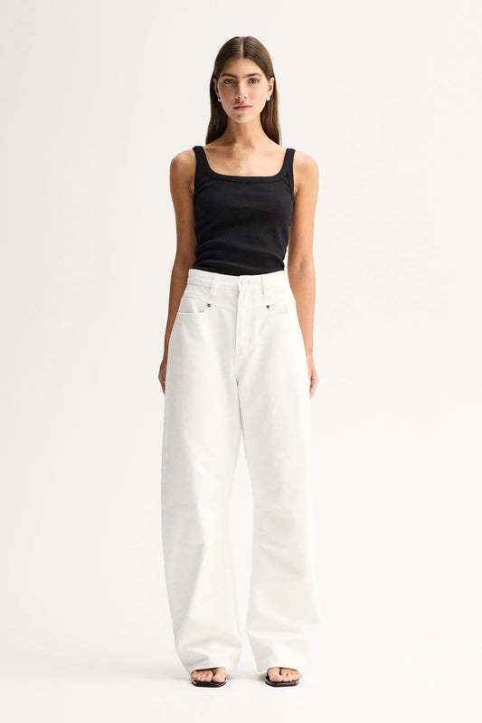 A woman modeling a black square-neck tank top and high-waisted, wide-leg white trousers against a plain white studio background.