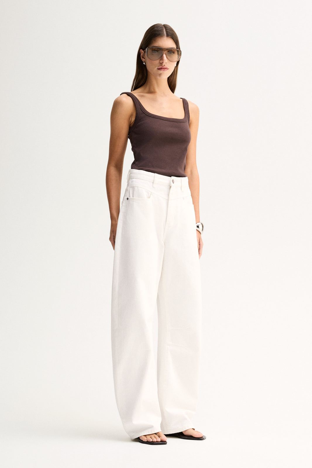 A woman wearing a chocolate fitted tank with white wide-leg pants, shown in a three-quarter front view.