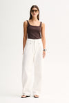 Front view of a woman wearing a chocolate ribbed tank with a low scoop neckline and white wide-leg pants.