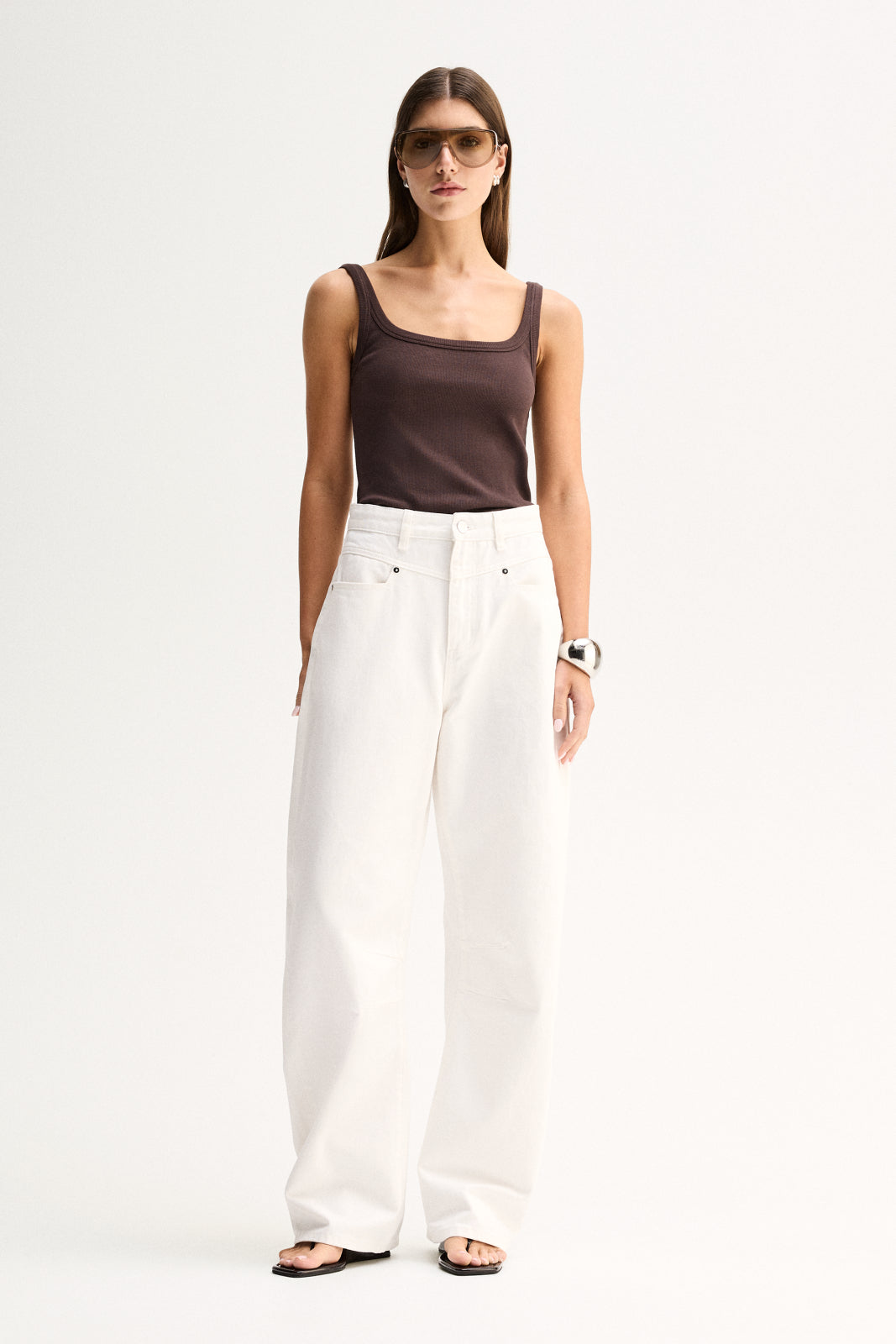 Front view of a woman wearing a chocolate ribbed tank with a low scoop neckline and white wide-leg pants.