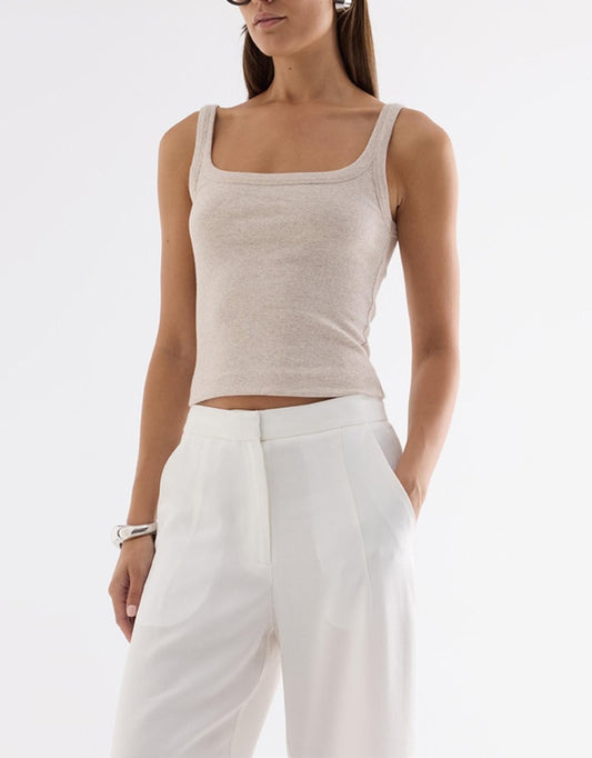 A woman wearing an Oatmarle fitted ribbed tank with a scoop neckline and thin shoulder straps, paired with white tailored pants.