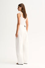 A woman wearing a white sleeveless jumpsuit with wide legs, shown from the back against a plain white studio background.