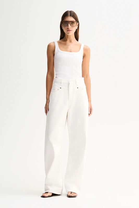 A model wearing a white sleeveless tank top and high-waisted white wide-leg jeans, styled with sunglasses and black slide sandals, against a plain white studio background.