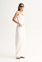 A woman modeling a white sleeveless camisole top paired with matching white wide-leg trousers, styled with dark sunglasses and black sandals against a plain white studio background.