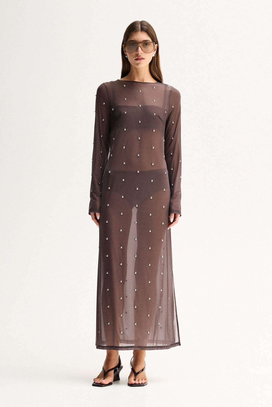 A woman wearing a slate sheer maxi dress with long sleeves, scattered stud details and a crew neckline in a full-length front view.