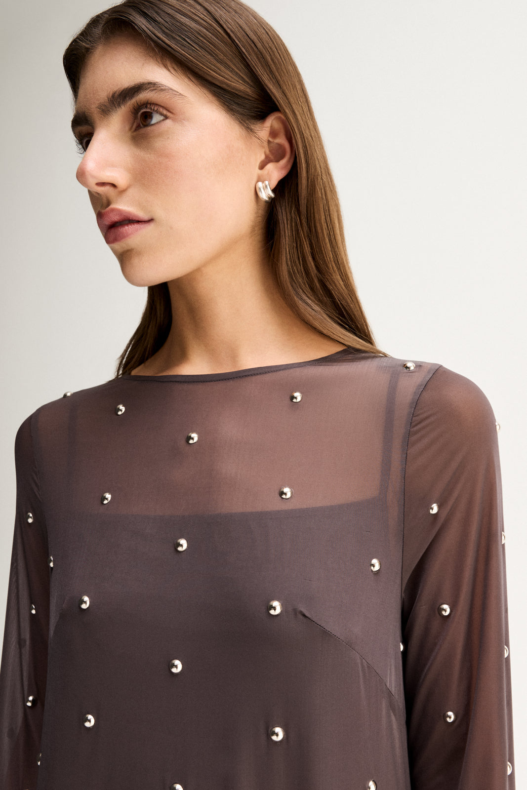 Close-up three-quarter view highlighting the sheer slate fabric, crew neckline and stud details across the upper body.