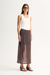 Three-quarter view of a woman wearing a slate sheer midi skirt with scattered stud details and a white sleeveless top.