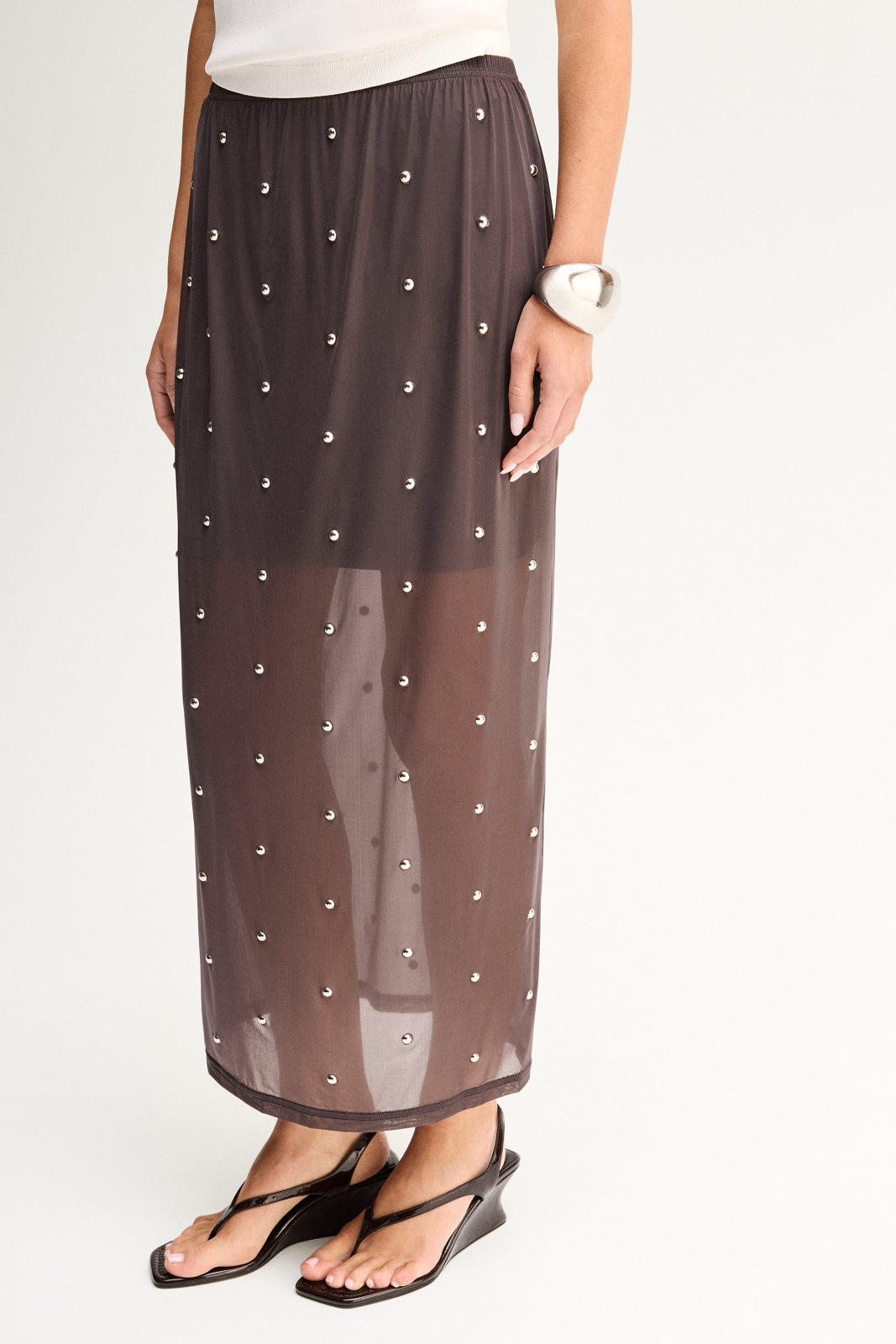 Close-up view showing the slate sheer fabric, scattered hot fix stud details, elasticated waistband and layered slip underneath.