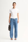 A model wears the Elka Collective Roxie Top in white with blue wide-leg jeans in a full-length front studio view.
