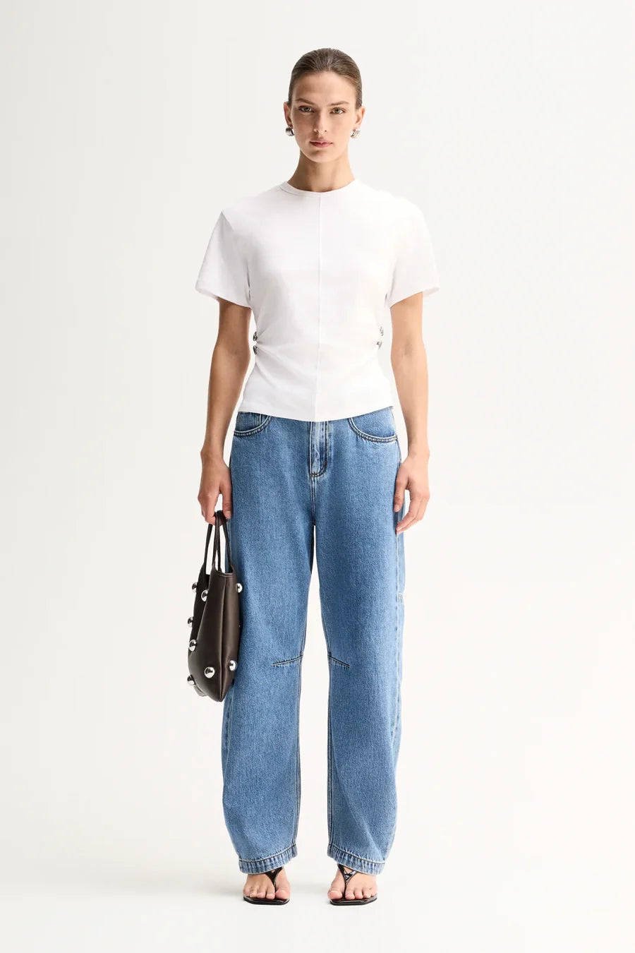 A model wears the Elka Collective Roxie Top in white with blue wide-leg jeans in a full-length front studio view.

