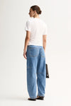 A model wears the white fitted top in a back studio view with blue wide-leg jeans.
