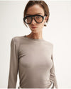 Model wearing the Almond Marle Sierra Top with oversized black sunglasses, showing the slim fit, long sleeves, round neckline and smooth fine-knit finish, close-up front view
