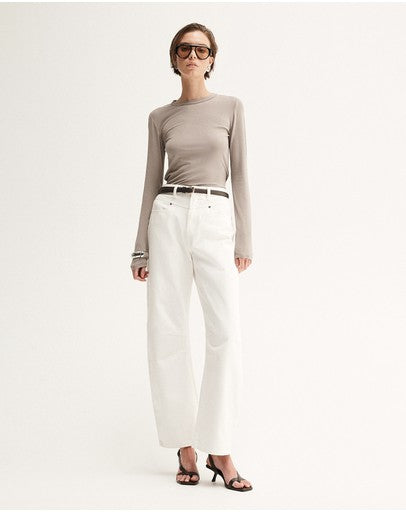 Model wearing the Almond Marle Sierra Top with white trousers and flat sandals, showing the slim silhouette, long sleeves and hip-length fit, full-length front view
