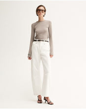 Model wearing the Almond Marle Sierra Top with white trousers and flat sandals, showing the slim silhouette, long sleeves and hip-length fit, full-length front view

