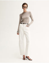 Model wearing the Almond Marle Sierra Top with white trousers, showing the fitted shape, round neckline and streamlined long sleeves, full-length front angled view
