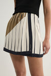 A close-up of the cream mini skirt showing fine dark vertical stripes, a diagonal moss and brown-toned panel across the upper section, gathered fabric at the waist and a wide dark border along the hem.
