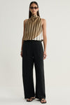 A model stands facing forward in a moss, cream and dark striped sleeveless top with a high neckline, tucked into wide-leg black trousers and paired with black sandals, showing the overall silhouette and full-length styling against a plain studio background.