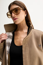 Close-up of the Camel Elka Collective Trixie Jacket worn open, showing the stand collar, plaid interior lining, zip front and silver-tone monogram hardware